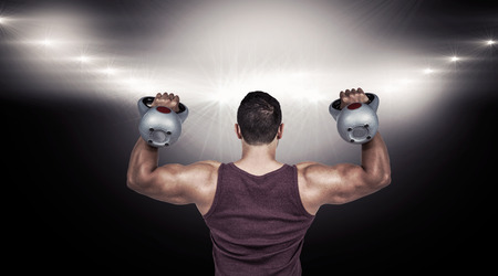 Rear view of a muscular man lifting kettlebells against lens flare