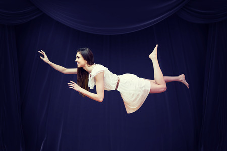 Girl in white dress floating in air against red curtainの写真素材