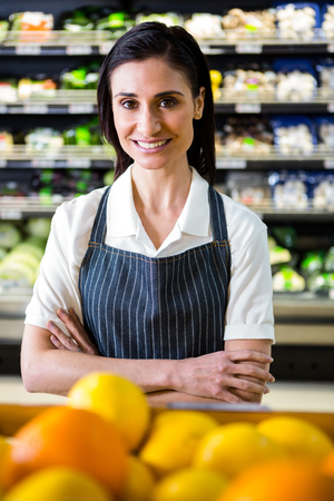 Pretty brunette looking at camera with arms crossed in supermarketの写真素材