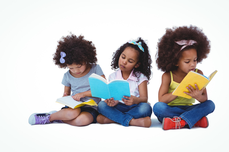 Cute girls sitting on the floor reading books on white screenの写真素材