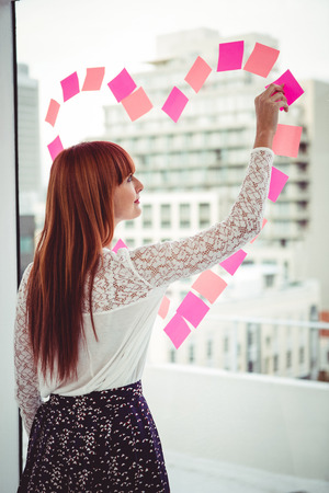 Rear view of a hipster woman doing a heart in post-it in officeの写真素材