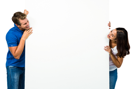 Smiling couple looking at each other behind board against white backgroundの写真素材