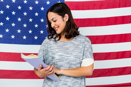 Smiling woman holding books while standing against America flagの写真素材