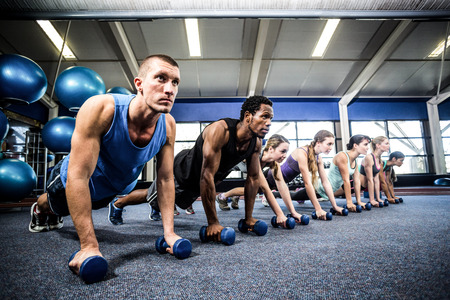 Fitness class in plank position with dumbbells at the gymの写真素材
