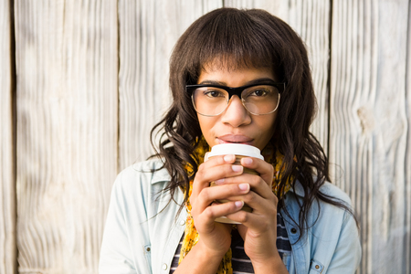 Smiling casual woman posing with glasses while drinking coffee against wooden plankの写真素材