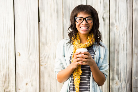 Smiling casual woman posing with glasses while holding coffee against wooden plankの写真素材