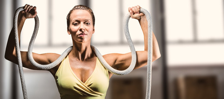Healthy woman holding rope around neck with arms raised against weights on the studio floor
