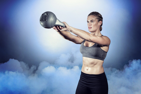 Muscular woman swinging heavy kettlebell against cloudy skyの写真素材