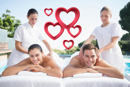 Smiling couple enjoying couples massage poolside against pink heartsの写真素材