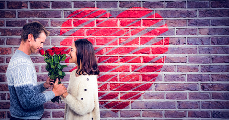 Romantic couple holding red roses against red brick wallの写真素材