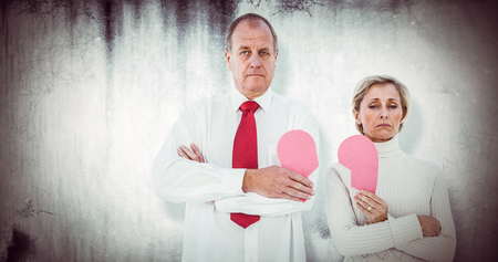 Older couple standing holding broken pink heart against grey backgroundの写真素材