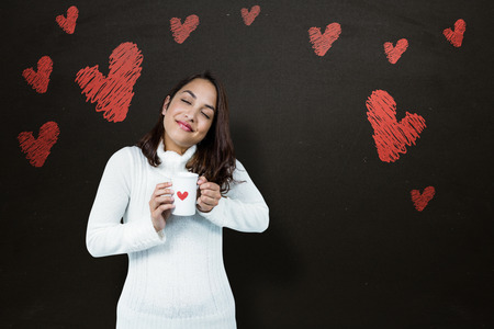 Beautiful woman holding coffee mug  against blackboardの写真素材