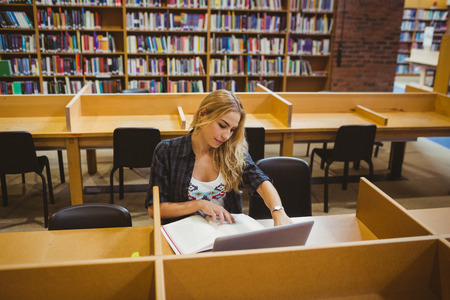 Smiling student working while using her laptop in library