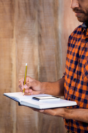 Businessman with smartphone writing on book against wooden wallの写真素材