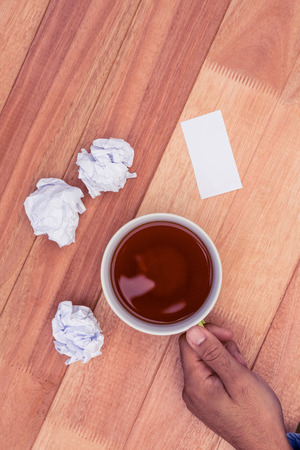 Cropped hand holding coffee cup by paper balls on desk in officeの写真素材