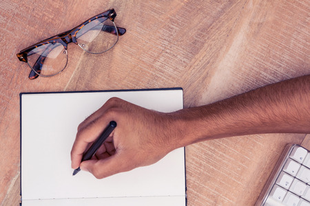 Cropped image of businessman writing on notebook by eyeglasses at desk in office