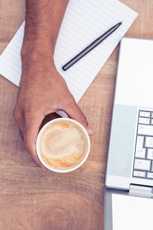 Overhead view of businessman having coffee while using laptop on desk in officeの写真素材