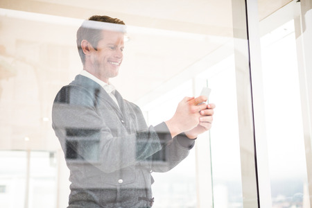 Cheerful man using mobile phone at office seen through glass windowの写真素材