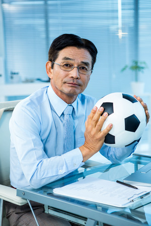 Asian businessman holding soccer ball in an officeの写真素材