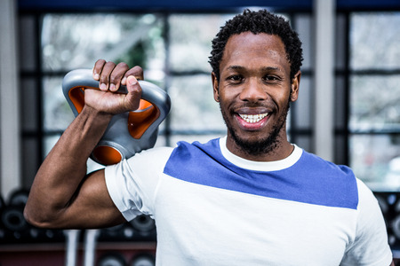 Smiling muscular man lifting kettlebells at gymの写真素材