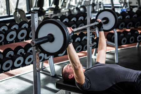 Muscular man lifting barebell while lying on bench at gymの写真素材