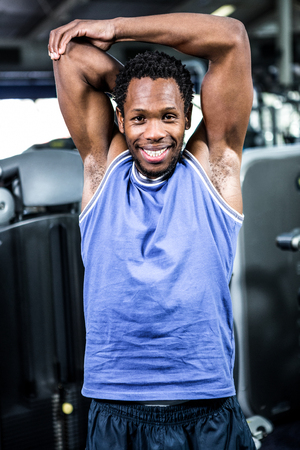 Smiling muscular man stretching arms at gymの写真素材
