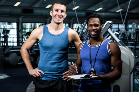 Muscular man with trainer smiling at camera at gymの写真素材