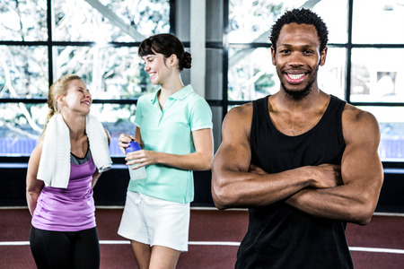 Smiling man with arms crossed while women chatting in crossfit