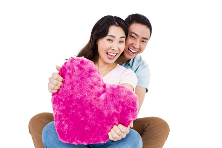 Portrait of cheerful young couple with heart shape pillow against white backgroundの写真素材