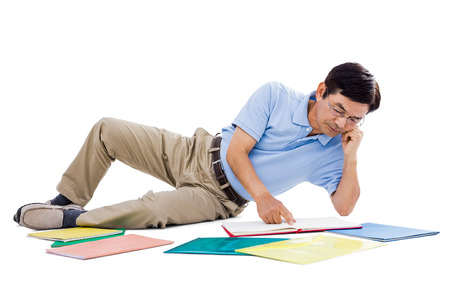 Smiling man reading books while lying on the groundの写真素材