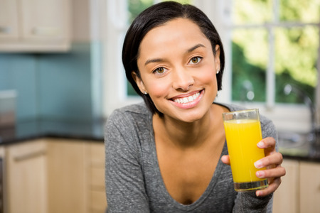 Smiling brunette holding glass of orange juice in the kitchenの写真素材