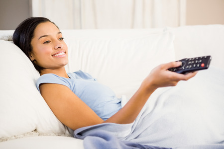 Smiling brunette using remote on the sofaの写真素材
