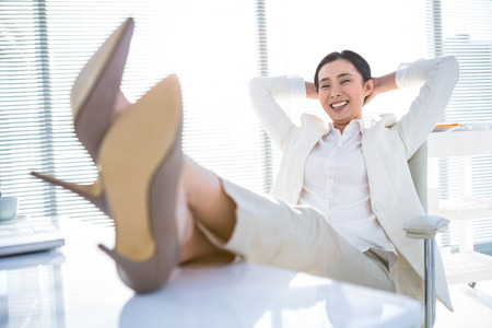 Relaxed businesswoman sitting with her feet up at deskの写真素材