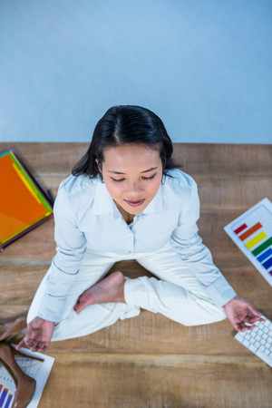 Peaceful businesswoman doing yoga sitting on floor with stuff aroundの写真素材