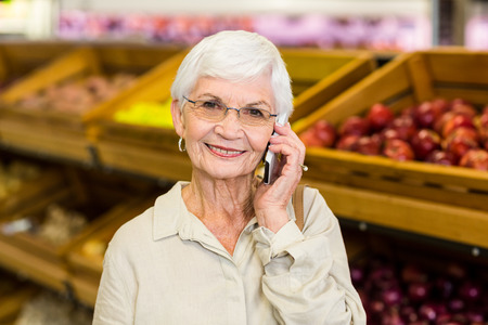 Old woman having a phone call in supermarketの写真素材