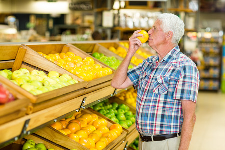 Smiling senior man smelling orange at the grocery shopの写真素材