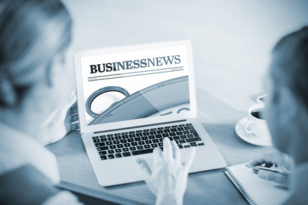 Close up on newspaper  against business people working together while using laptopの写真素材