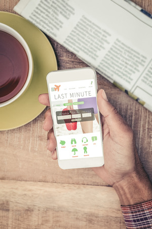 Man using smart phone by coffee and newspaper on table against holidays booking appの写真素材