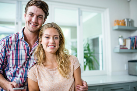 Cute couple smiling and texting in the kitchenの写真素材