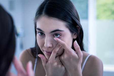 Brunette putting her contact lens in bathroomの写真素材