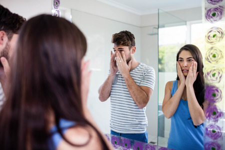 Couple looking themselves in the mirror in bathroomの写真素材