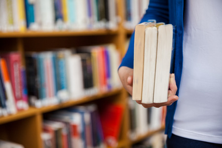 Happy female student taking books in the library at the universityの写真素材