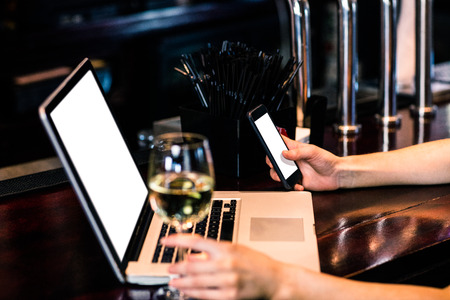 Woman texting and using laptop with wine in a barの写真素材