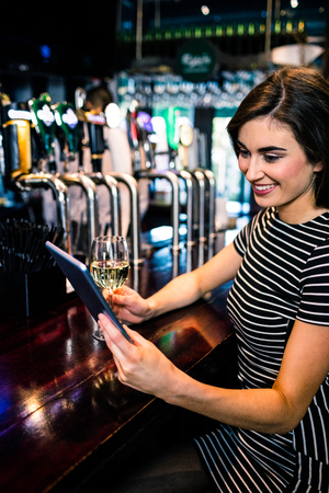 Woman using tablet and having a glass of wine in a barの写真素材