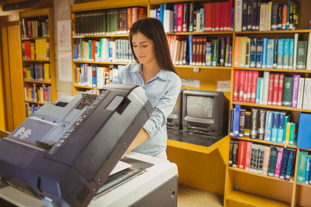 Smiling brunette student making a copy in libraryの写真素材