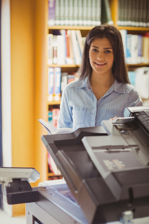 Smiling brunette student making a copy in library