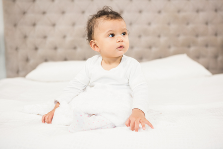 Cute baby sitting on bed looking aroundの写真素材