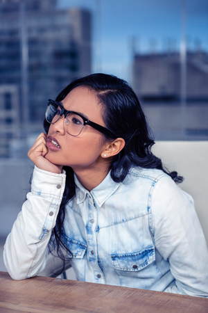 Troubled Asian woman with chin on fist in officeの写真素材