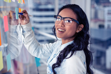 Asian woman writing on sticky notes on glass wallの写真素材