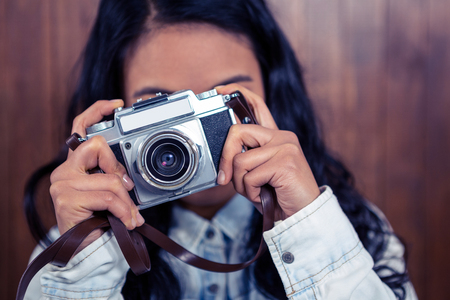 Asian woman taking picture with digital camera against wooden wallの写真素材